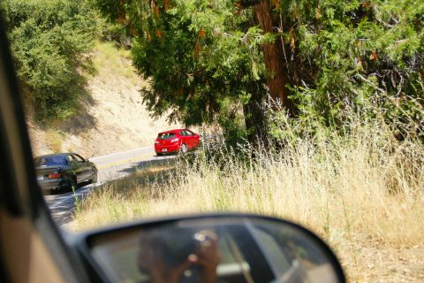 1995 Ford Taurus - A red hatchback navigates a curve on a tree-lined road, with another car visible ahead.