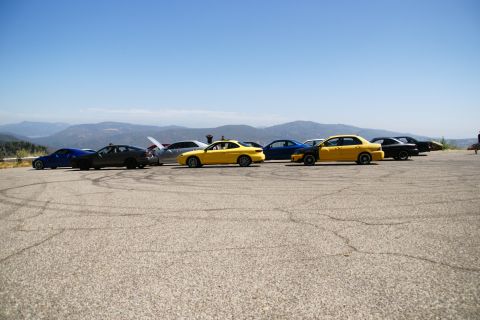1995 Ford Taurus - A group of cars are parked on a paved surface with a scenic mountain backdrop under a clear sky.