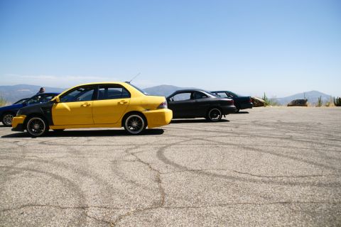 1995 Ford Taurus - Several cars are parked on a lot with tire marks, with a yellow sedan in the foreground.