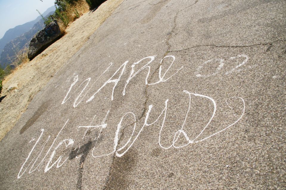 White chalk writing on asphalt reads 'WARE UP WATFORD'. Hills in background