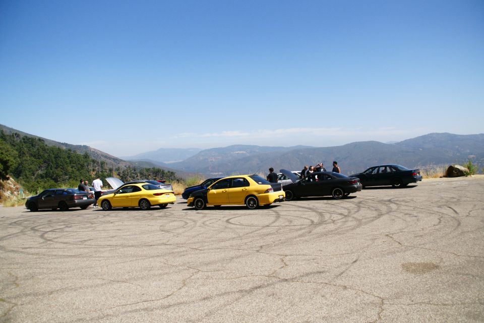 Several cars parked on a paved area with tire marks, overlooking a mountain range