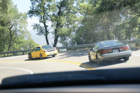 1995 Ford Taurus - Two cars navigate a sharp curve on a scenic mountain road.