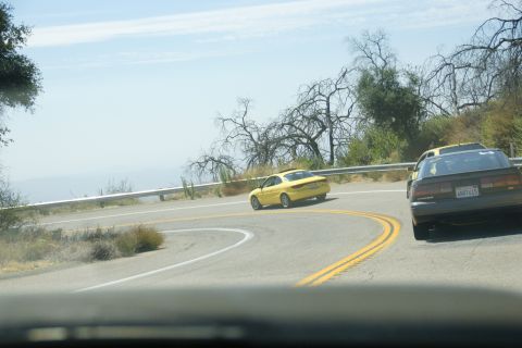 1995 Ford Taurus - Two cars navigate a sharp curve on a scenic mountain road under a clear sky.