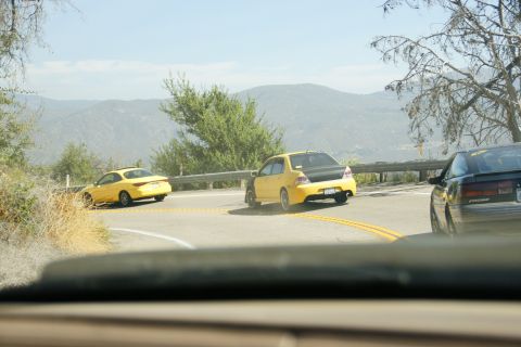 1995 Ford Taurus - Three cars, two yellow sedans and one dark coupe, navigate a mountain road.