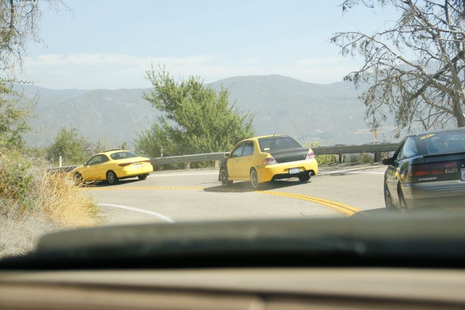 Yellow sedan with a black trunk lid driving on a winding road