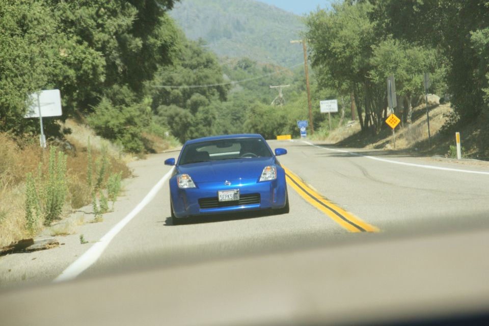 Blue sports car driving on a two-lane road with trees and hills in the background