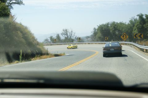 1995 Ford Taurus - Two cars navigate a sharp curve on a scenic mountain highway under a clear sky.