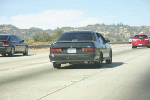 1995 Ford Taurus - A dark 1995 Ford Taurus is seen from behind on a sunny day, driving on a highway with other vehicles.