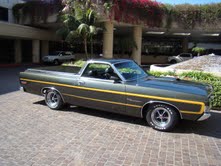 1979 Ford Ranchero - A green Ford Ranchero pickup truck is parked in front of a building with palm trees.