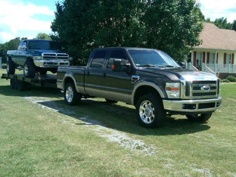 1997 Dodge 2500 - A Ford F-Series truck tows a Dodge Ram pickup on a trailer in front of a house.