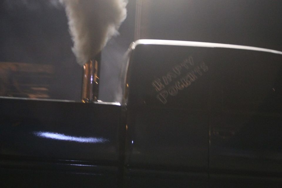 Side view of a truck with a large exhaust pipe emitting smoke and the words "Empty Pockets" on the door
