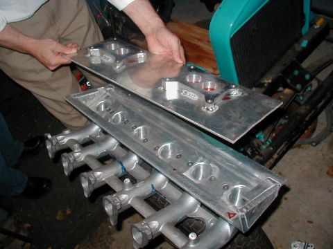 1981 Ford Bronco - A person holds a fabricated aluminum plenum lid with twin carburetor/throttle-body flanges above a six-runner cast intake manifold with an…