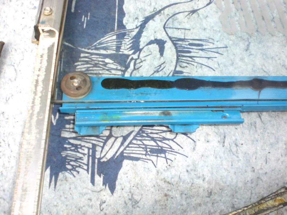 Blue window regulator rail with roller resting on a crane-patterned blanket next to a metal trim strip