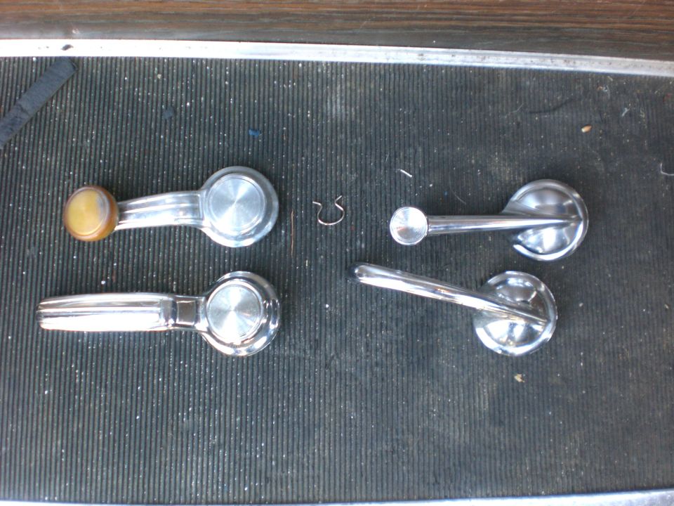Four chrome window crank and door handles with a small retaining clip on a black ribbed mat