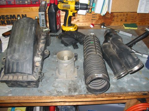 1992 Ford Bronco - Ford air intake components are laid out on a workbench, including a filter housing, throttle body, and intake hose.