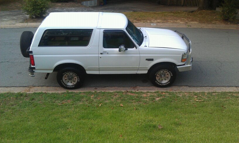 White Ford Bronco parked on a street, side view. Spare tire mounted on the back