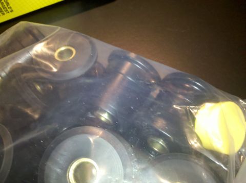 1998 Ford Crown Victoria - clear plastic bag filled with black and yellow polyurethane bushings and metal sleeves rests on a dark surface near a yellow label.