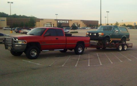 1989 Ford Bronco - A red pickup truck tows a green 1989 Ford Bronco on a trailer in a parking lot.