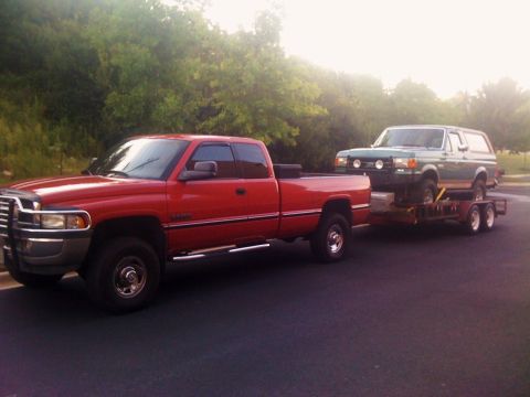 1989 Ford Bronco - Red Dodge Ram pickup truck towing a green Ford Bronco on a trailer.