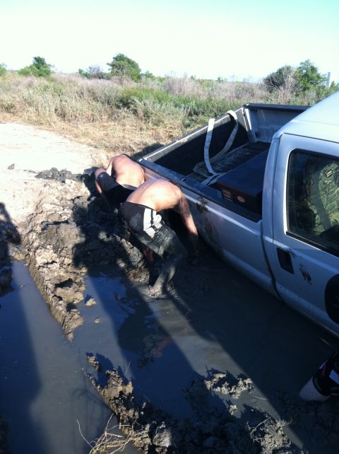 1994 Ford Bronco - Two individuals struggle to free a silver pickup truck from a muddy ditch.