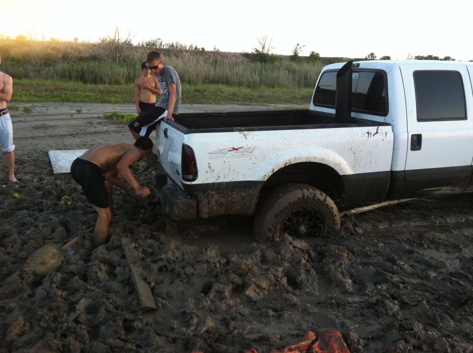 White pickup truck stuck in mud with people trying to free it