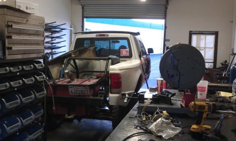 1992 Ford Ranger - A 1992 Ford Ranger is parked in a workshop, showing a custom bed with a large fuel tank and roll cage.