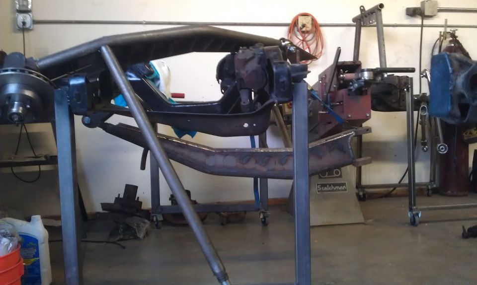 Vehicle frame on stands in a workshop, showing suspension components and custom tubing