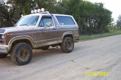 1982 Ford Bronco - This muddy Ford Bronco, likely from the early 1980s, is driving on a dirt road.