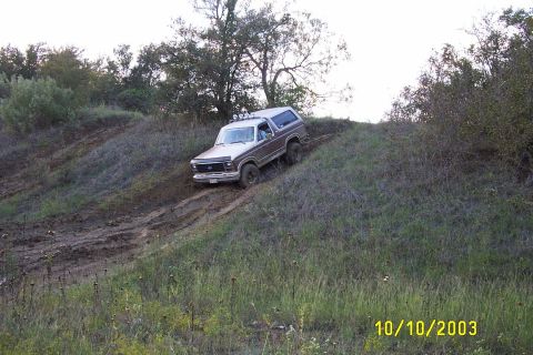 1982 Ford Bronco - This classic Ford Bronco is navigating a challenging off-road trail with steep inclines and muddy patches.