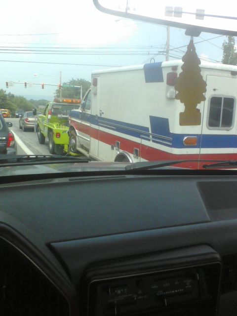 1988 Ford Bronco - A tow truck is transporting an ambulance on a road, seen from another vehicle's perspective.