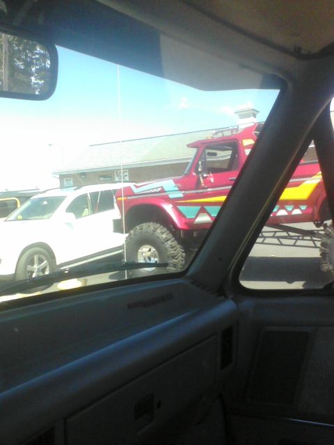 1988 Ford Bronco - A lifted red truck with custom graphics is parked next to a white SUV.