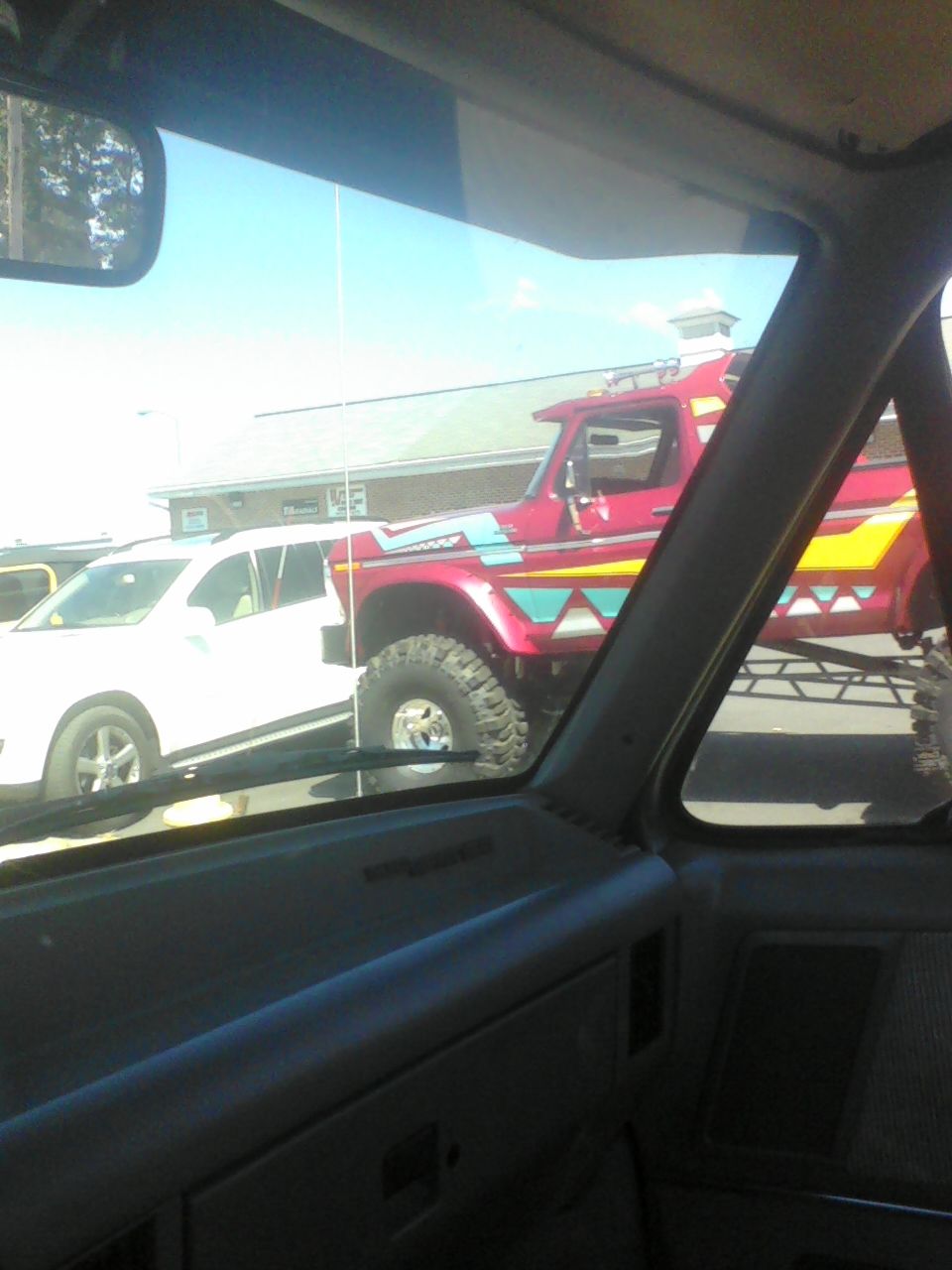 Red lifted truck with yellow and blue geometric graphics parked next to a white SUV