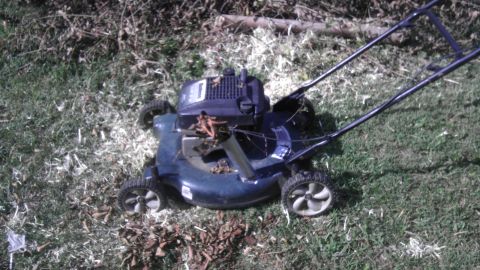 1989 Ford Bronco - A dark blue lawn mower sits on a patch of grass, surrounded by cut grass clippings and fallen leaves.