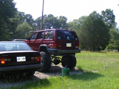 1978 Ford Bronco - A heavily modified Jeep Cherokee sits high off the ground next to a Volvo sedan in a grassy area.