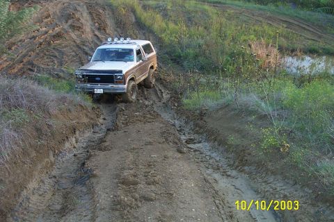 1982 Ford Bronco - A Ford Bronco navigates a muddy track with overhead lights visible.