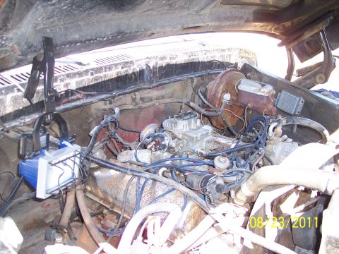 1978 Ford Bronco - The engine bay of a vehicle, showing the carburetor and various engine components, with a work light attached.