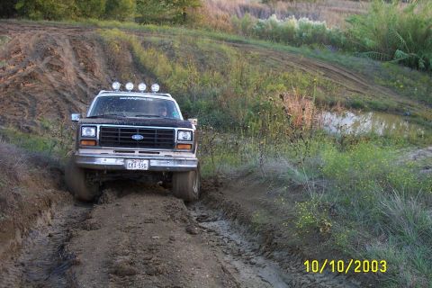 1982 Ford Bronco - A Ford Bronco navigates a challenging muddy terrain, kicking up dirt as it goes.