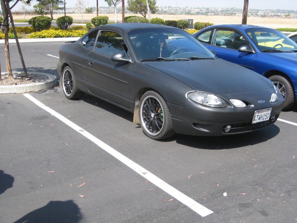 Dark gray Ford Escort coupe parked in a lot. Blue car next to it