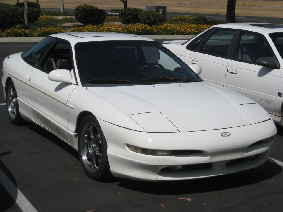 White 1990 Ford Probe coupe with pop-up headlights parked next to another white car