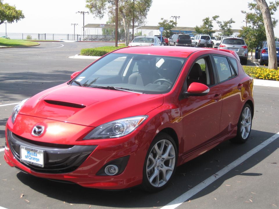 Red Mazda hatchback parked in a lot. License plate reads "Mazda of Orange"