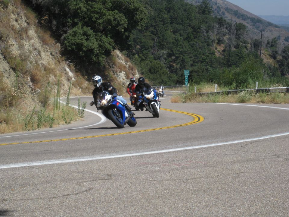 Sportbike riders leaning through a mountain highway curve led by a blue and white GSX-R
