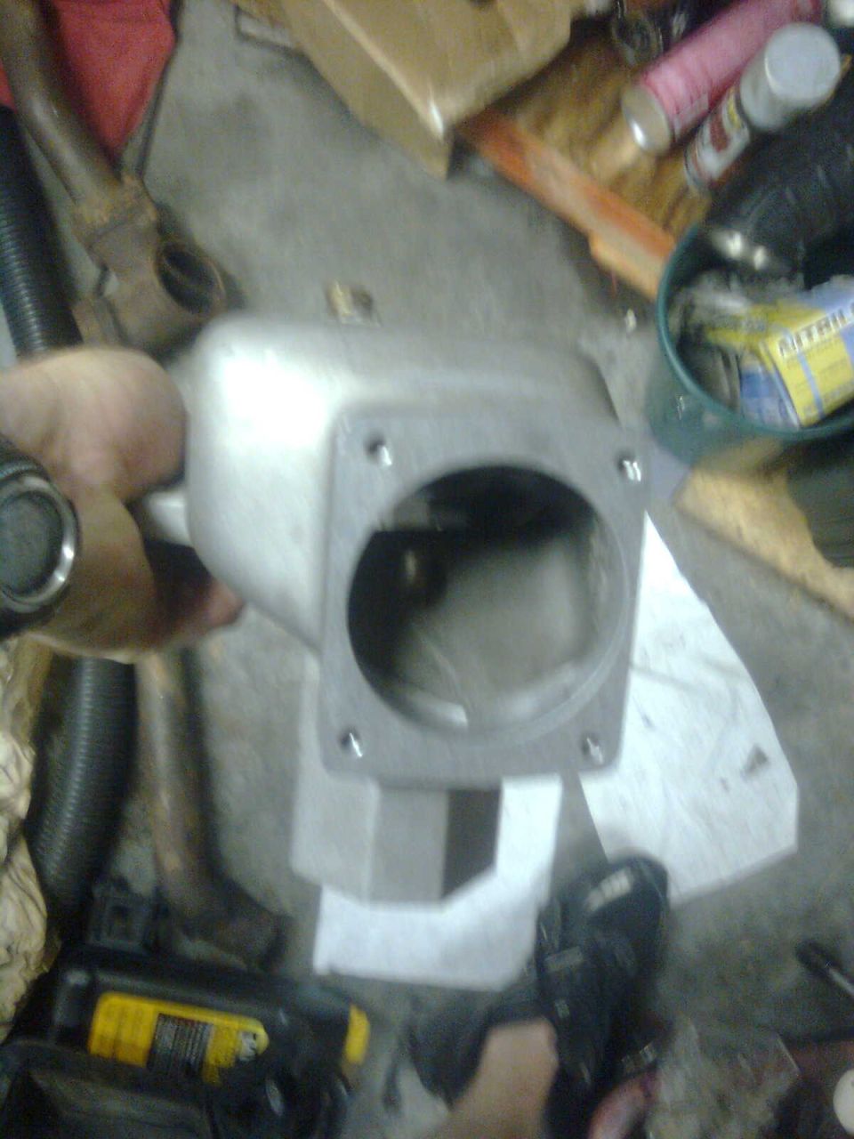 Hand holding a cast aluminum throttle body or intake elbow over a shop floor