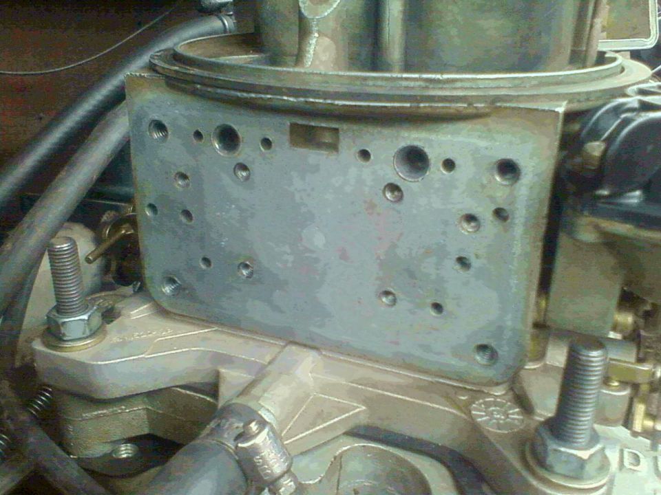 Side of a carburetor body on aluminum intake manifold with mounting studs and brass fittings