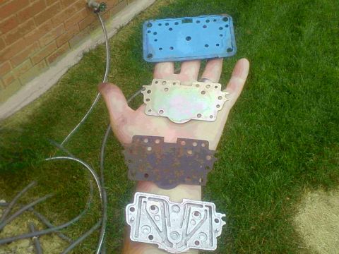 1981 Ford Bronco - A collection of carburetor base plates are displayed on a hand against a grassy background.