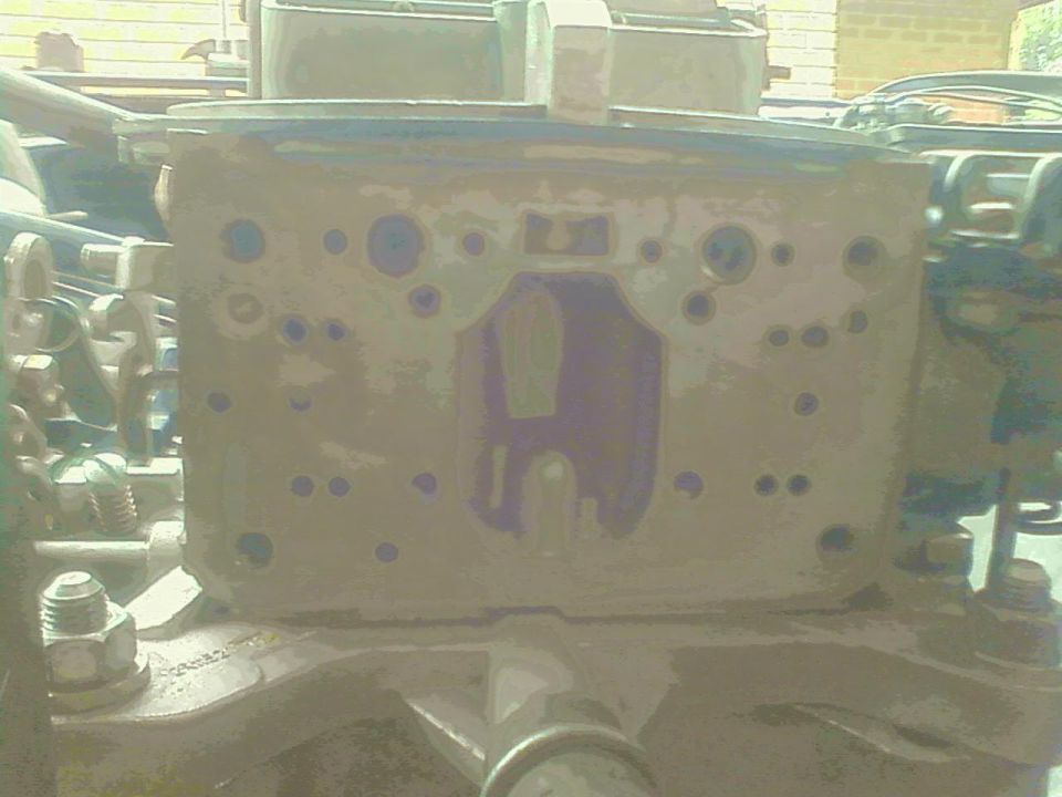 Carburetor with a purple H-shaped marking and numerous bolt holes