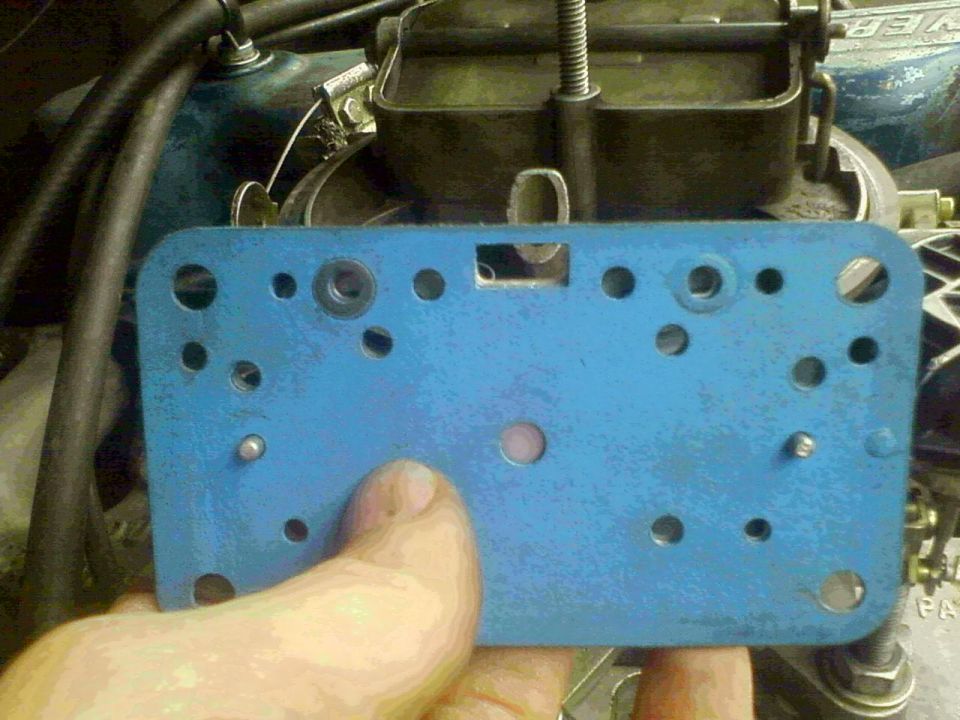 Blue carburetor spacer plate held in front of engine components
