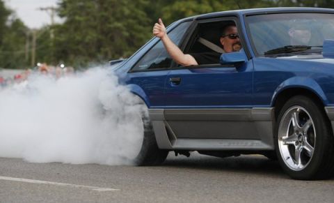 1990 Ford Mustang - A blue 1990 Ford Mustang performs a burnout, with the driver giving a thumbs up.