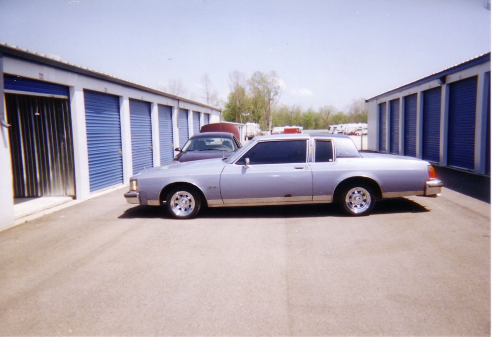Silver-blue two-door coupe, driver's side view, parked by storage units