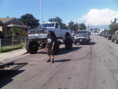 1986 Ford Bronco - A heavily modified white pickup truck with oversized tires is parked on a residential street.