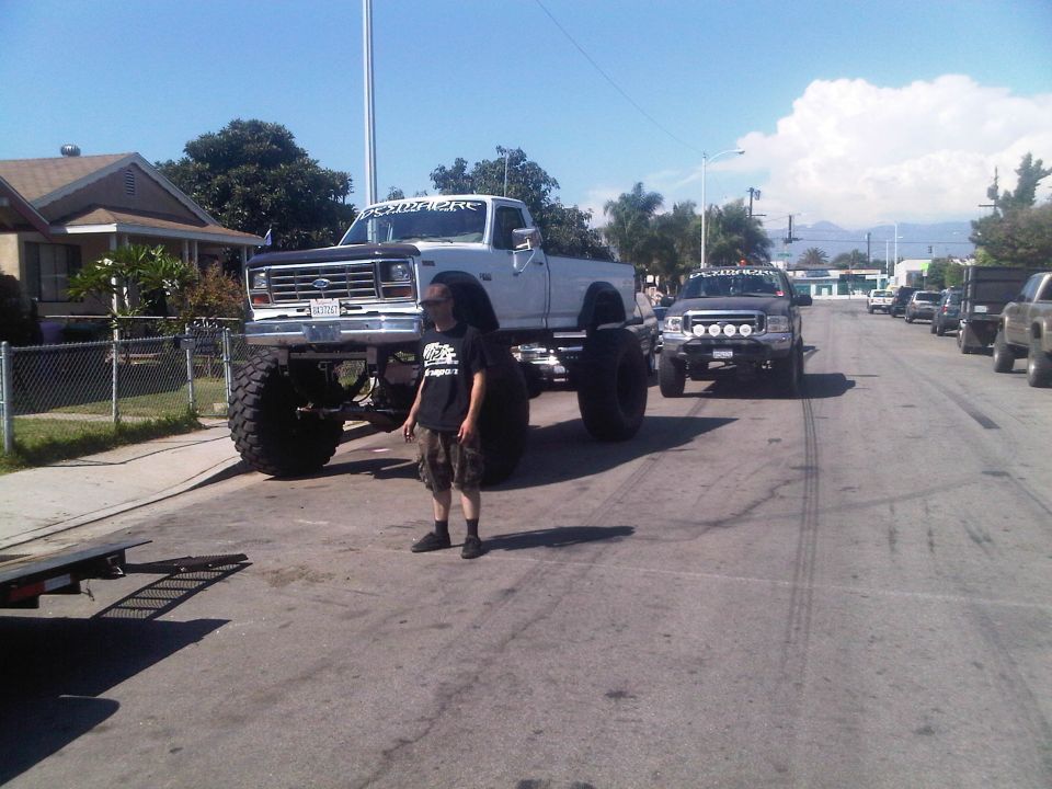 White lifted pickup truck with large tires, front view. A person stands nearby